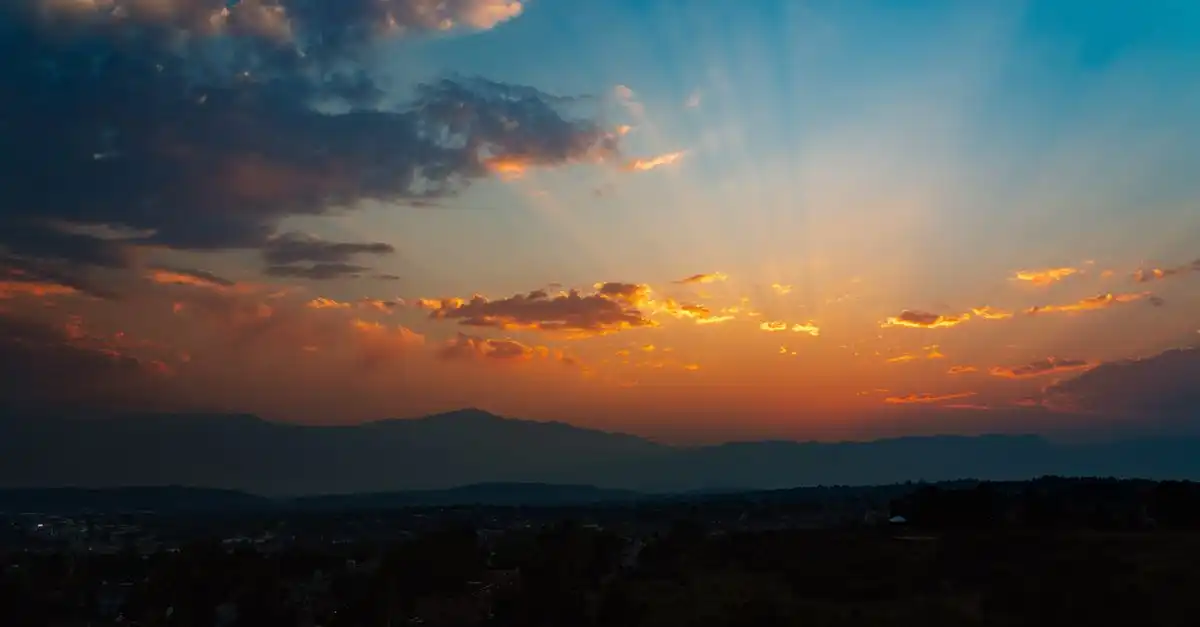 A mountain ridgeline at sunrise above Colorado Springs, cloud bands lit orange over the valley
