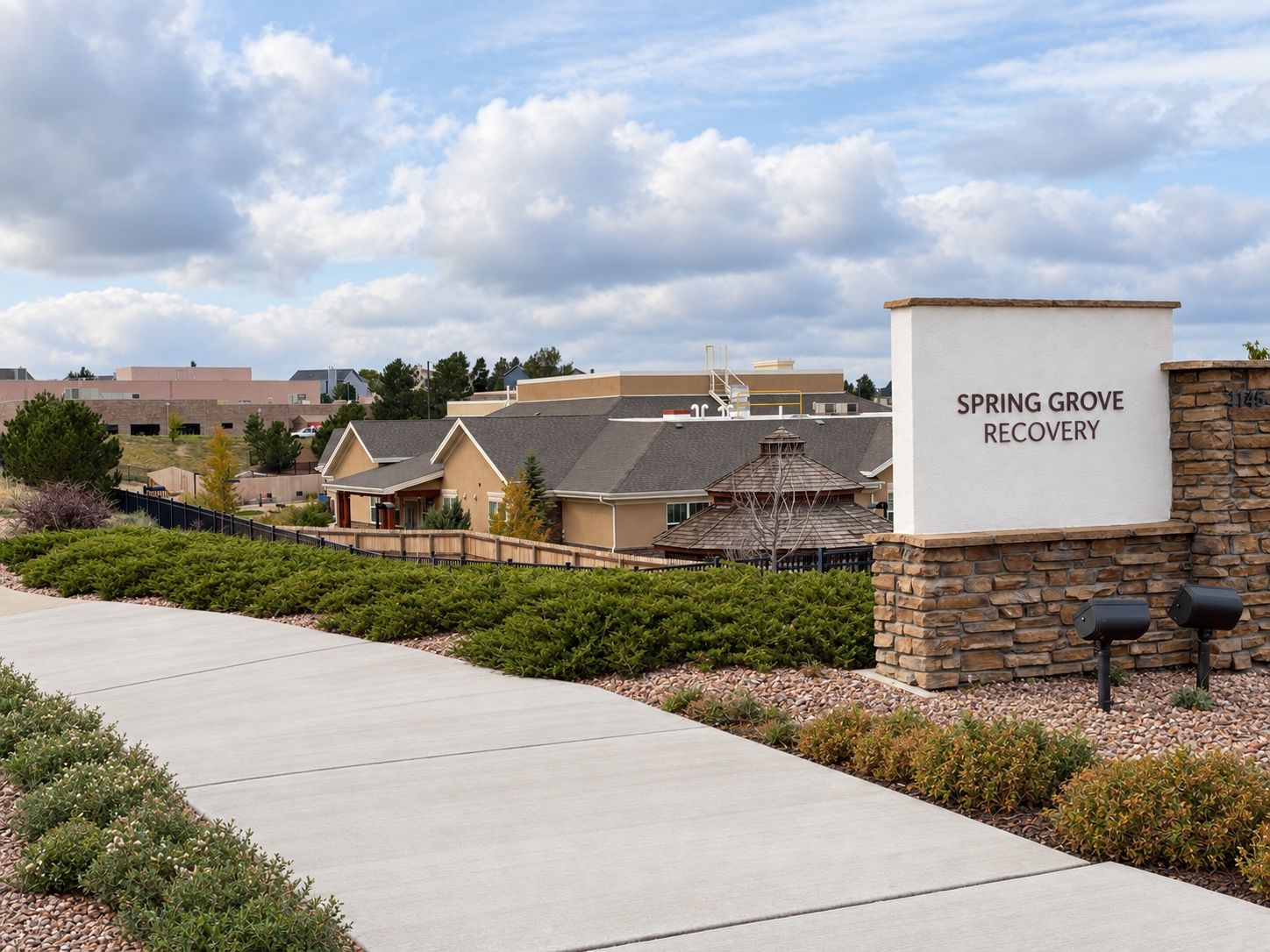 The Spring Grove Recovery monument sign beside a walkway, with the campus buildings behind it