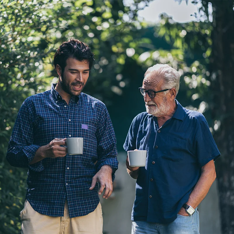 one younger man and one older man each have a cup of coffee outside as they discuss what to expect in addiction treatment