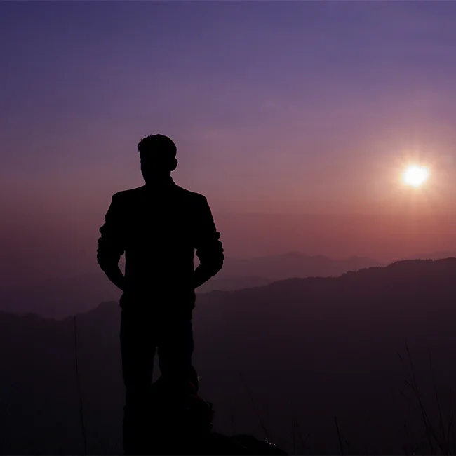 a man stands at the top of a hill range at dusk