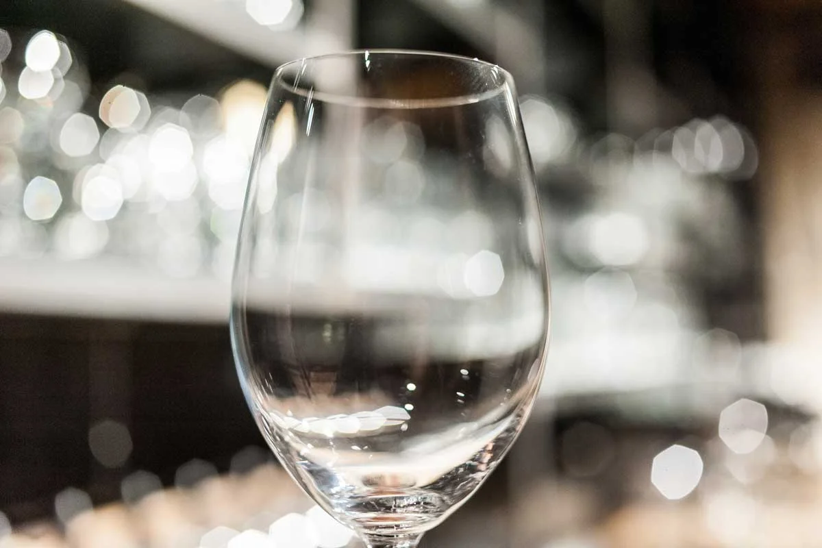 An empty wine glass sits on a bar. The background is blurred.